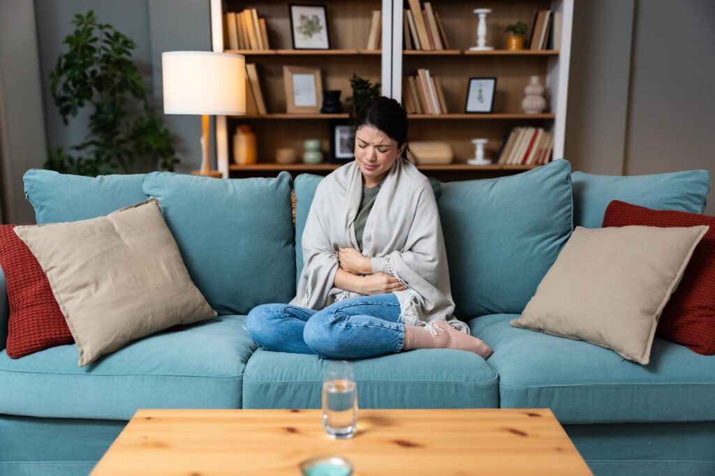 woman sat on a sofa with her feet up clutching her stomach