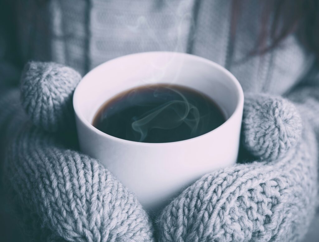 hands in woollen mittens holding a ug of drink