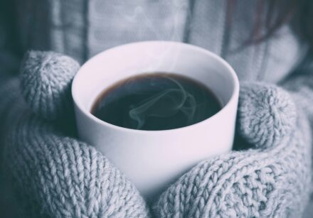 hands in woollen mittens holding a ug of drink